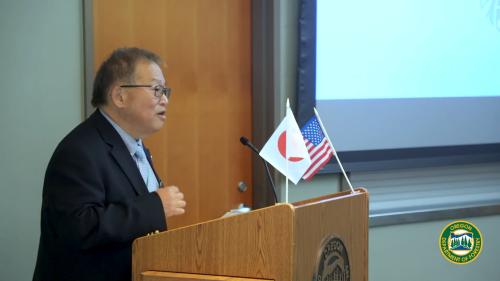 A women stands behind a podium with Japanese and American flags